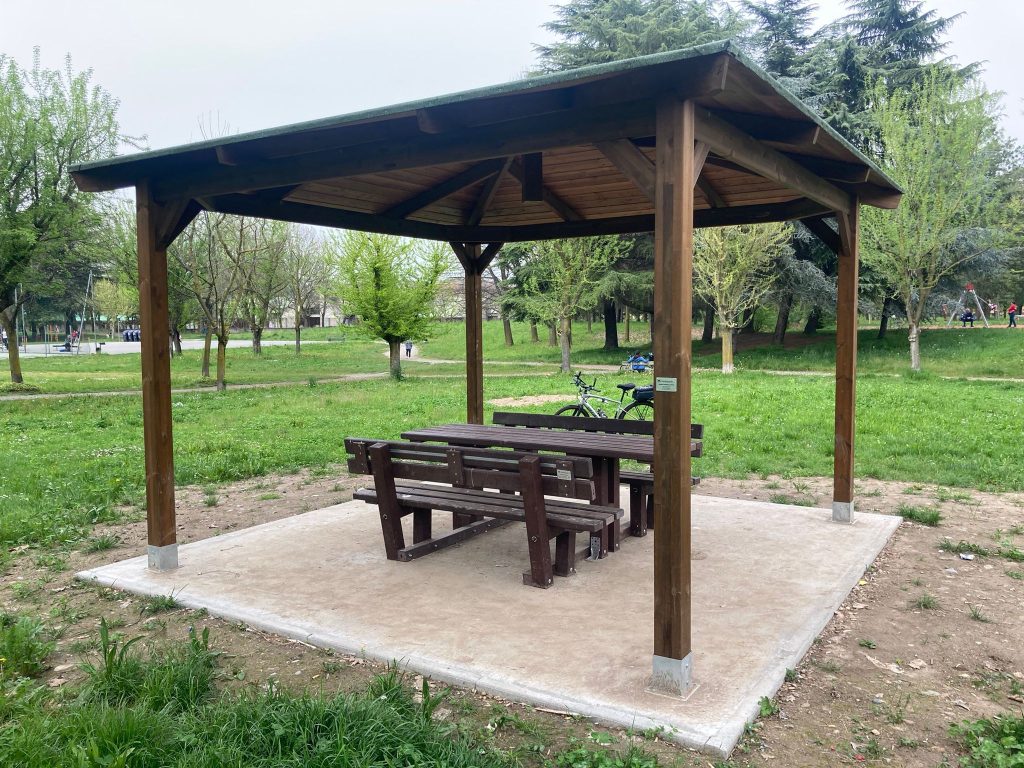 Gazebo per le aree verdi, in legno lamellare con doppia impregnazione. Tavolo da picnic in plastica riciclata al 100%, panche con schienale.
